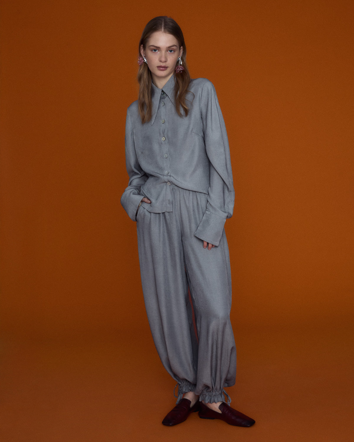 Soft grey oversized blouse with a gentle ruffled collar and relaxed silhouette, photographed against a clean neutral background