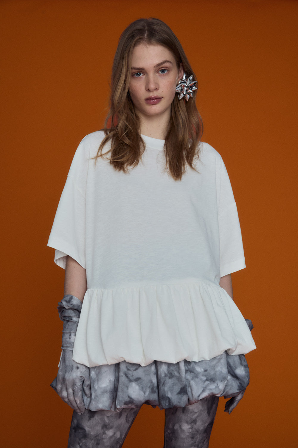 A soft oversized white tee with a clean, minimalist shape, photographed against a neutral background. The fabric drapes lightly, giving a cloud-inspired airy look