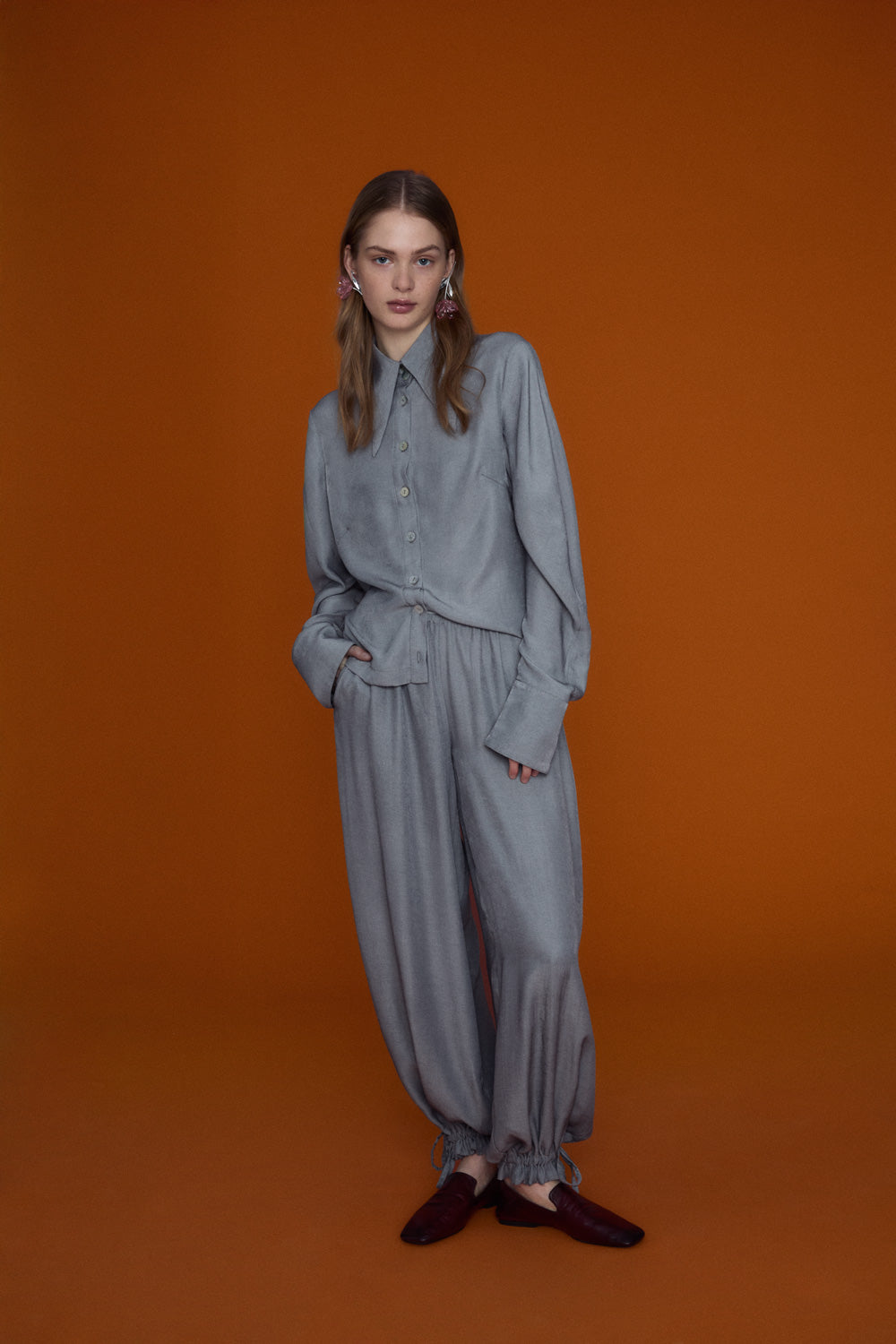 Soft grey oversized blouse with a gentle ruffled collar and relaxed silhouette, photographed against a clean neutral background