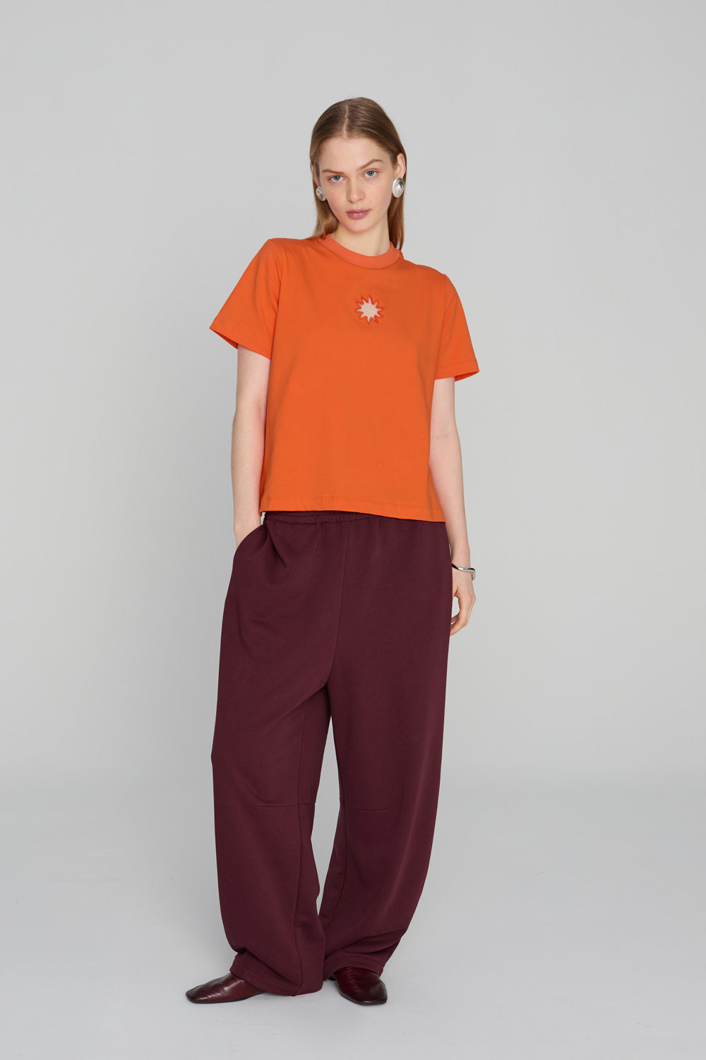 Bright orange oversized T-shirt with a clean minimalist silhouette and soft draping fabric, photographed against a neutral background.