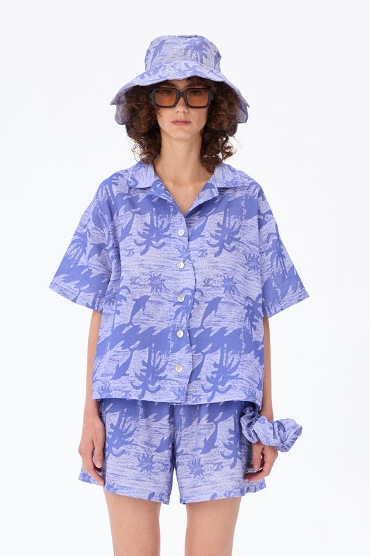 “Loose-fitting short-sleeve shirt in 100% cotton with an exotic dolphin and palm-tree print and mother-of-pearl buttons, styled on a neutral background.”