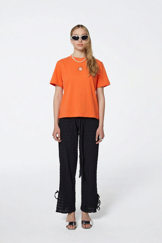 Bright orange oversized T-shirt with a clean minimalist silhouette and soft draping fabric, photographed against a neutral background.